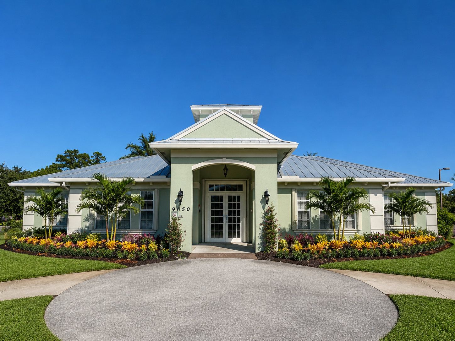 Seafoam green commercial building with curved driveway, manicured tropical planting beds, and palm trees maintained by SPS